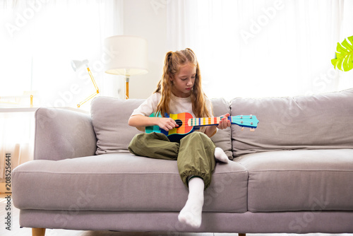 Young Girl Playing Colorful Toy Guitar on Sofa at Home