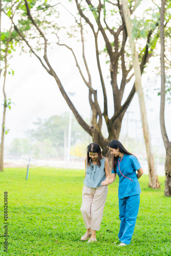 Fototapeta premium Full length of smiling young asian nurse walking and holding hands with happy senior woman at the park, Elder care concept.