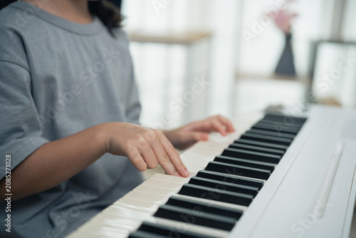 Child practicing piano with focused hands pressing keys on white keyboard in bright indoor environment learning music instrument