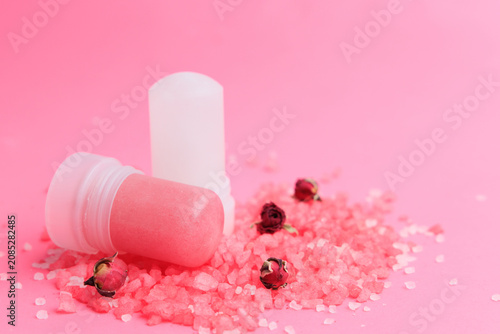 Natural crystal alum deodorant placed on pink salt with small dried flowers on a light pink surface for a beauty and wellness theme