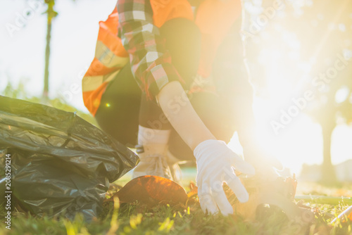 Obraz na plátne Volunteer cleaning activity in a sunny park, collecting waste into a garbage bag