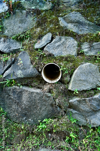Foto A detailed view of an old circular drainage pipe embedded within a rugged stone retaining wall covered in moss and small green plants