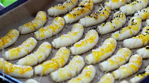Hands Sprinkling Sesame Seeds and Spices on Homemade Bread Rolls in Baking Tray Before Baking