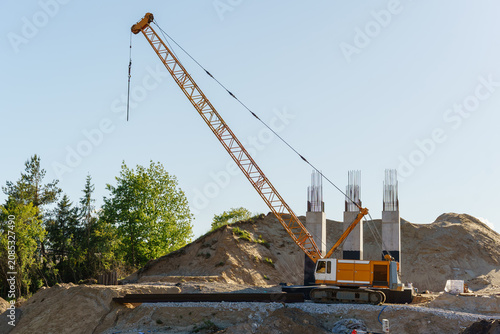 Fotografie Large yellow crawler crane on an active construction site with bridge supports a