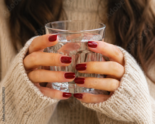 Woman in beige sweater holding a glass of clear water