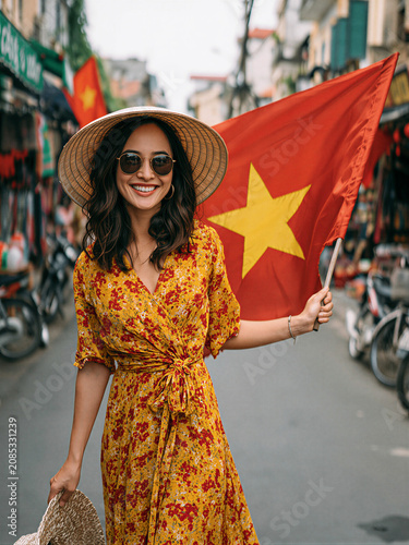Smiling young woman holding Vietnam flag in narrow city street