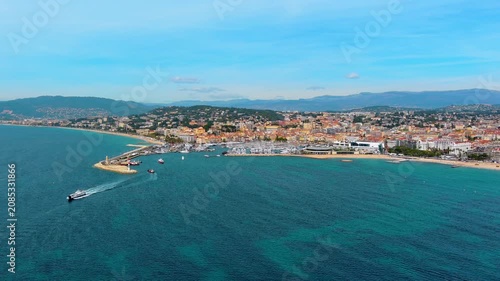 Aerial view of the bay of Cannes, France, with a boat entering the old port past the lighthouse jetty, moored yachts, the Palais des Festivals, La Croisette beach and hills of the French Riviera.