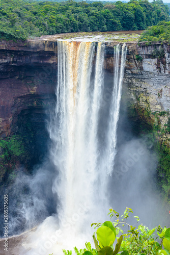 High waterfall cascading over a rocky cliff surrounded by lush green tropical rainforest vegetation with waterfall