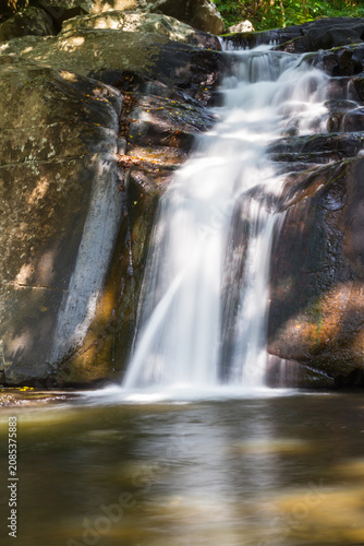 Close up vertical view of rushing water flowing down rocky tiers in a shaded forest with waterfall landscape outdoors