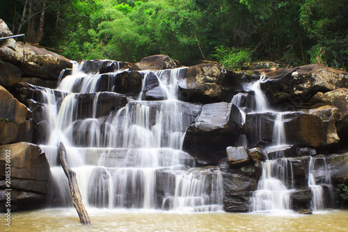Small multi-tiered rocky waterfall cascading through dense tropical forest greenery with waterfall cascading tropical
