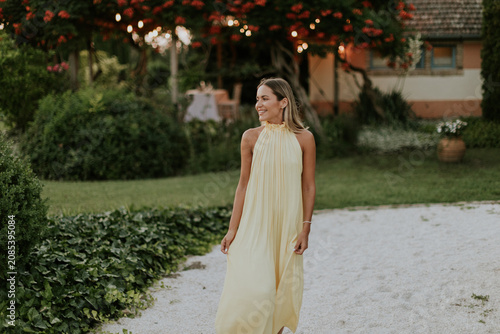 Woman in a flowing yellow dress strolls in a serene garden setting