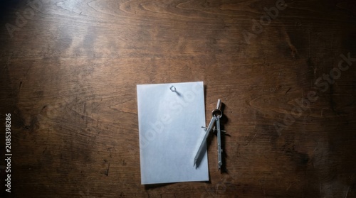 Blank white vellum paper sheet pinned to a dark wooden drafting board with a metal compass tool for architectural design