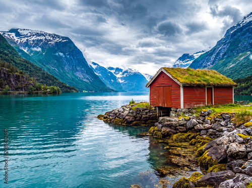 Foto Traditional red boathouse with a green grass roof by a pristine Norwegian fjord
