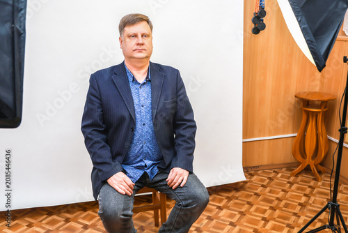 A man sits on a chair in a photo studio, preparing for a photo shoot for documents and a passport.