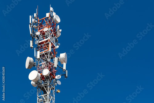Telecommunication mast equipped with advanced 5G cellular antennas and microwave sector dishes for high-speed wireless network transmission, isolated on clear blue sky backdrop,   with copy space