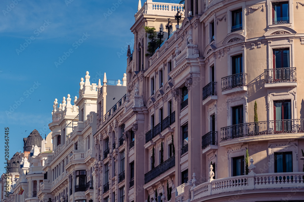 Obraz premium Elegant row of historic neoclassical facades along Gran Via under a blue sky in Madrid