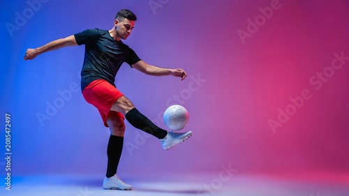 Professional soccer player juggling a ball in studio against a vibrant blue and pink neon gradient background