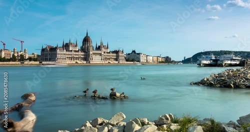 Budapest skyline timelapse along the Danube river featuring the Hungarian Parliament Building under moving white clouds on a sunny day