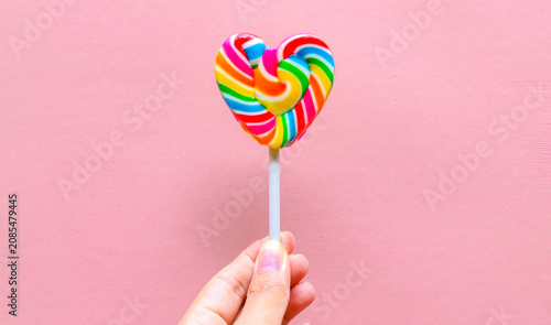 Tableau sur toile Hand holding colorful heart shaped lollipop isolated on pink background
