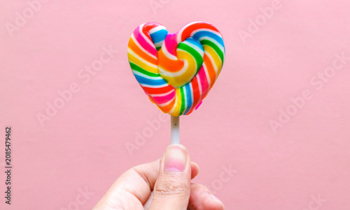 Tableau sur toile Hand holding colorful heart shaped lollipop isolated on pink background