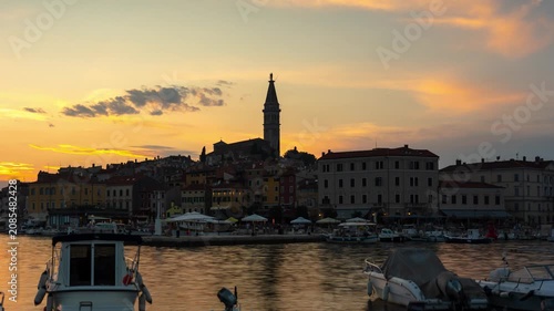 Rovinj old town harbor time lapse during a vibrant golden hour sunset with moving clouds, passing boats, and the historic church tower in Croatia