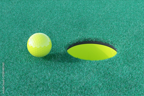 Bright yellow golf ball near empty modern hole on green grass surface in cont...