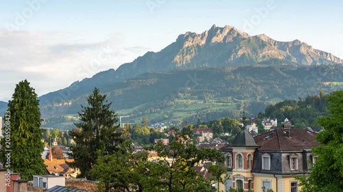 Time lapse of Mount Pilatus with moving shadows and golden hour sunlight casting over Lucerne cityscape and lush green Swiss hills