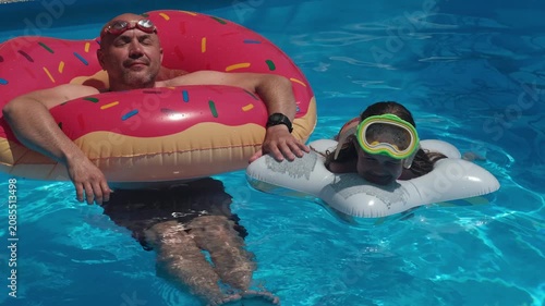 Happy smiling man in donut float and girl in diving mask swimming in pool. Concept of family summer vacation