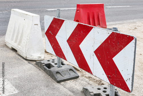 Red and white chevron barrier marks road construction zone. Temporary traffic equipment protects work area. Roadwork background for safety, detour and infrastructure repair.