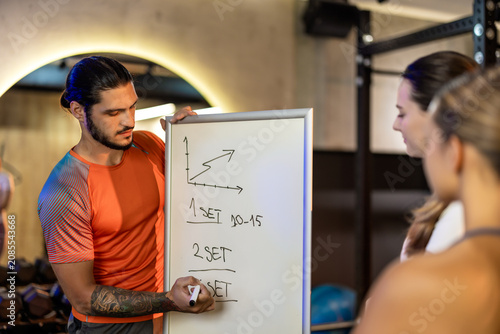 Foto Two athletic women listening to a personal trainer writing a fitness program on a whiteboard