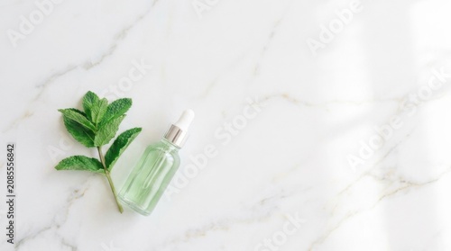 Natural mint essential oil or serum in glass dropper bottle with fresh mint leaves on white marble background with copy space