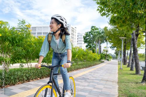 Asian woman wears headphones listening to music while cycling to work.