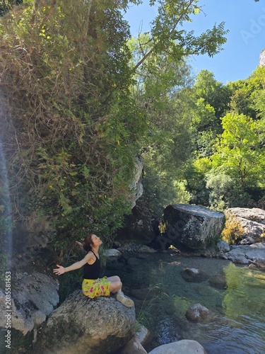 Woman sitting on a rock by the river with arms wide open enjoying nature and freedom
