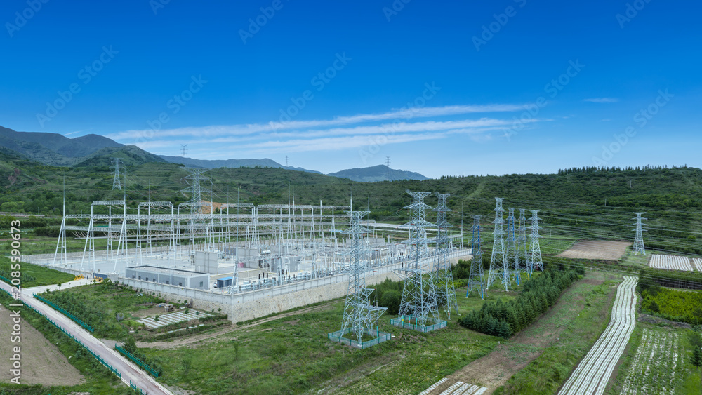 Fototapeta premium Modern Substation with Transmission Towers Amid Green Hills and Farmland