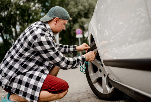 Bild auf Leinwand Man squats, connecting air pump to white car tire valve on pavement outdoors during day