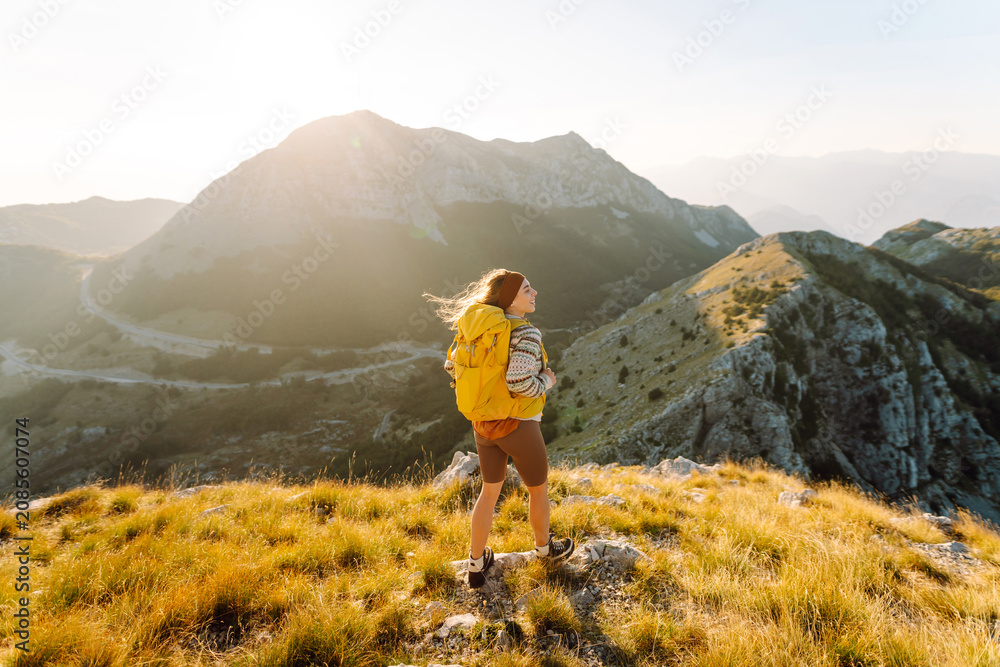 Obraz premium Female hiker with backpack on edge of a mountain feels free. Hiker enjoys the mountain scenery and walks along hiking trail in mountains. Concepts of hiking, adventure, and nature.