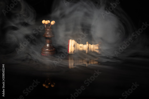 Fotografie Dark chess queen standing over fallen white queen in dramatic swirling smoke on black background