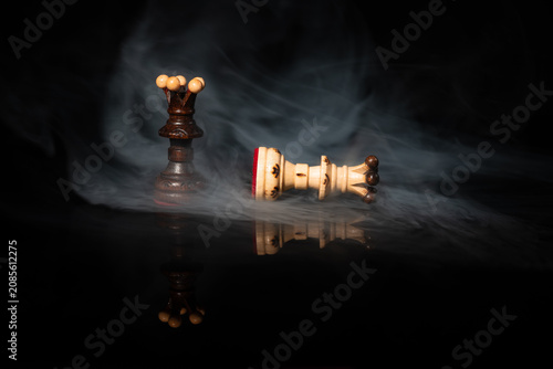 Fotografie Dark chess queen standing over fallen white queen in dramatic swirling smoke on black background