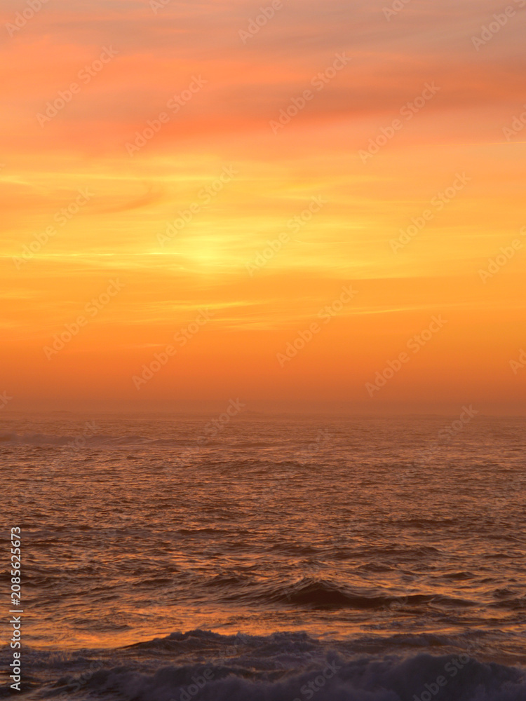 Obraz premium Sunset over the ocean. The light from the setting sun casts beautiful orange and golden hues onto the altostratus-type clouds.