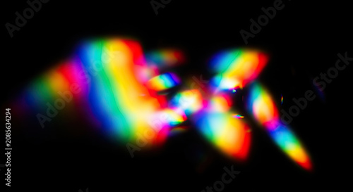 A vibrant, multicolored light display is projected onto a dark background. The light creates a dynamic, abstract pattern of rainbow hues, resembling a shimmering, distorted lens flare.