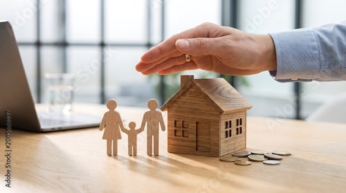 Hand Protecting Wooden House And Family Figurines On Desk For Home Insurance Financial Security Real Estate Investment