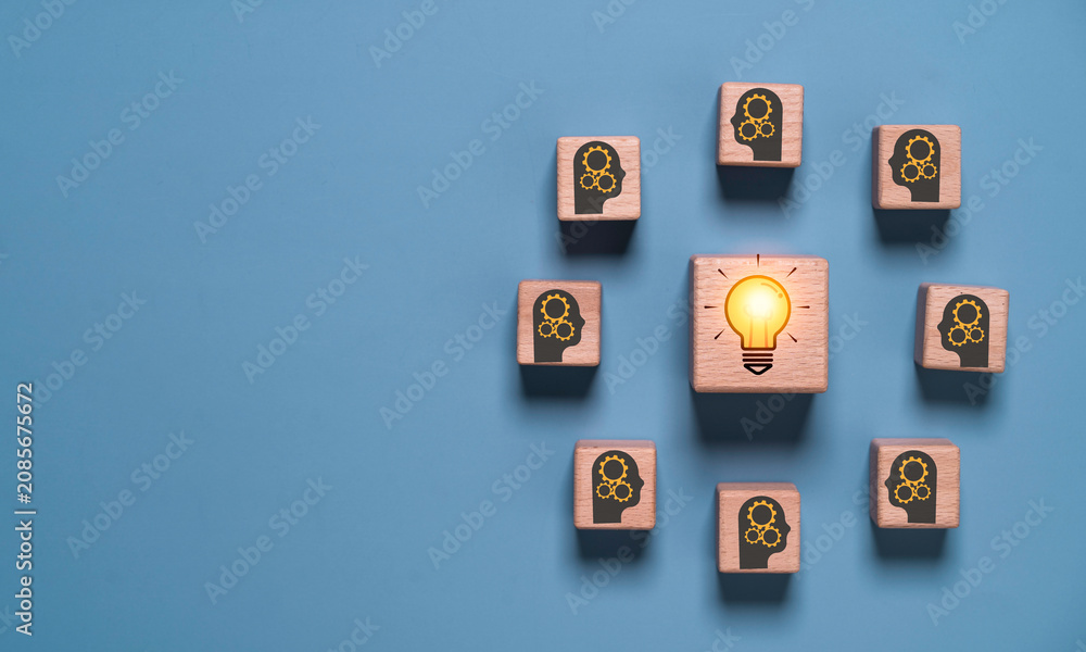 Fototapeta premium Wooden blocks with human head icons surrounding a glowing light bulb, symbolize teamwork, innovation, brainstorming, creative thinking, knowledge sharing, problem solving and business collaboration.