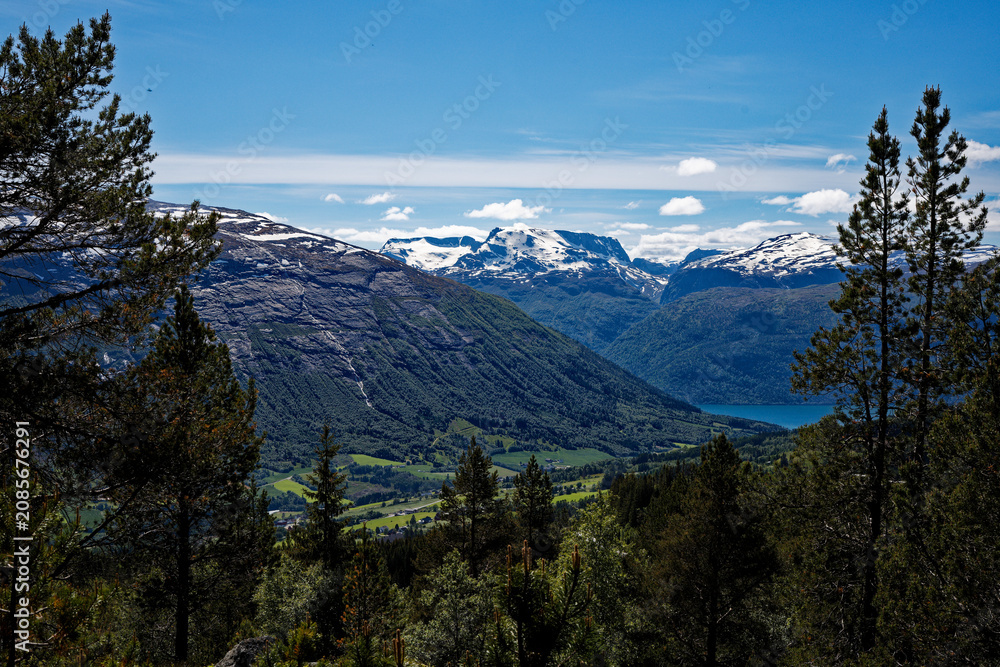 Obraz premium Norwegian mountain vista: snow peaks, lush valley, blue lake, vibrant pine trees