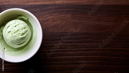 Single scoop of green ice cream in a white bowl on a dark wooden table.