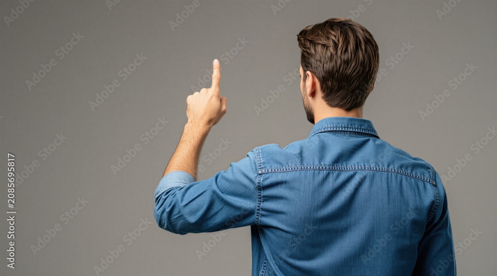 Obraz premium Man in denim shirt points finger up. Back view of person indicating choice or idea, perhaps making a selection or offering guidance. Casual gesture, focused on action.