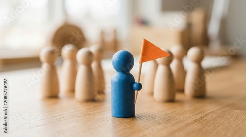 Blue wooden figure holding an orange flag leading a group of plain wooden figures on a table in a professional business leadership concept