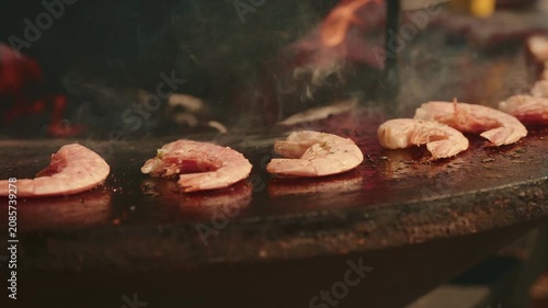 Grilled shrimp cooking on a round metal outdoor barbecue grill. Seafood preparing on hot surface. Culinary process of roasting crustacean for delicious meal.