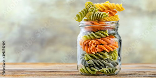 Colorful spiral pasta stacked in a glass jar on a wooden table Generative AI