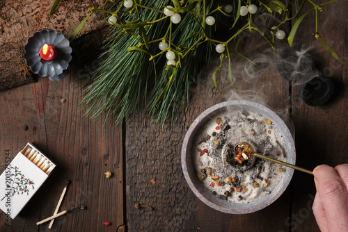 Frankincense and dried herbs burning on glowing charcoal - placing incense with a spoon