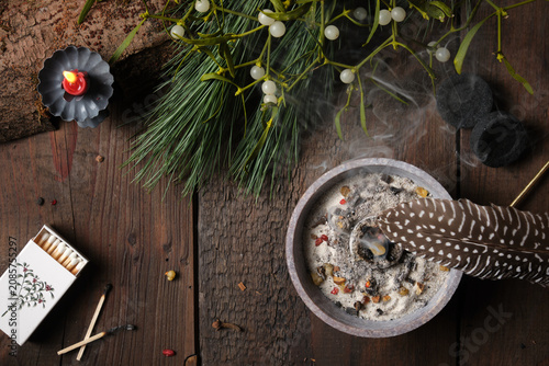 Incense burning on glowing charcoal with dark background - spreading smoke with a feather